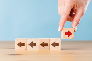 Woman hand holding block with red arrow facing the opposite direction other arrows. Think...