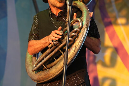A man playing a tuba on an outdoor stage illuminated by sunlight.Player in action close-up