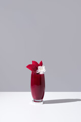 Un vaso de jugo de remolacha decorado con rodajas de remolacha sobre una mesa blanca y fondo gris	