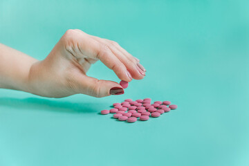 Female hand holding  pink pills. Turquoise background. Close-up view