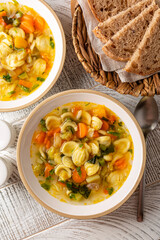 Minestrone soup with pasta orecchiette and seasonal vegetables. on a light table, top view. Delicious vegetarian italian food concept. Flat lay, vertical image.