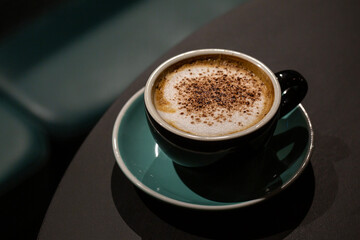 A cup of caffe cappuccino with cocoa chocolate powder. Coffee drink with steamed milk foam. Dark green background.