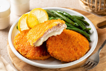 Close-up of plate with fried chicken Cordon bleu with melted cheese and ham, in breadcrumbs, green beans and lemon.