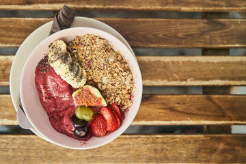 Top view of smoothie bowl with fresh fruit, berries and muesli on the background of a wooden table. Healthy vegetarian breakfast. High quality photo