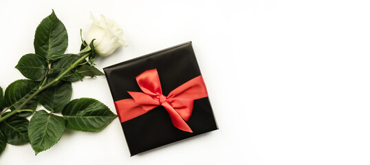 White rose with green leaves on a white background. Gift box with a bow. Holiday concept.