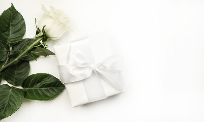 White rose with green leaves on a white background. Gift box with a bow. Holiday concept.