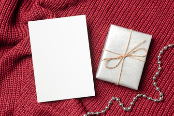 Blank greeting card mockup with gift box on red knitted background