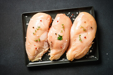 Chicken breast with spices at black background. Raw meat ready for cooking. Top view.