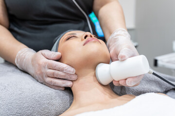 Beauty therapist treating young woman skin on neck with modern device in spa