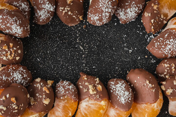 Orange juicy tangerine slices covered with melted milk chocolate on black concrete background. Sweet appetizer