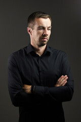 Portrait of man in a black shirt on a dark background. Serious brunet with arms folded. Young caucasian man