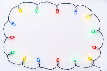 Christmas theme. Multicolored illuminated garland in retro style on a white wooden background with copy space. The garland is arranged in the form of a frame.