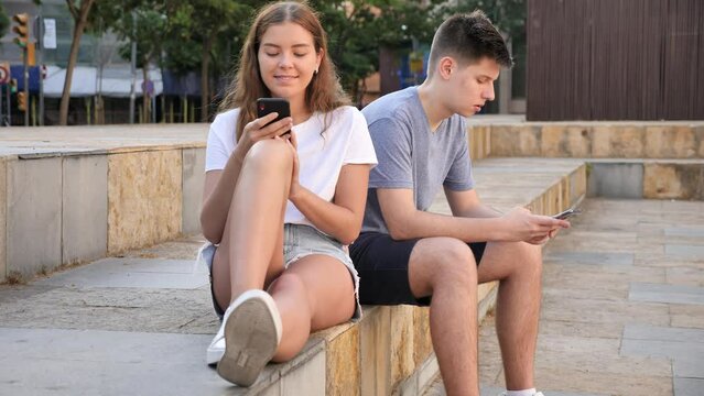 A coulpe of teenagers with smartphones is sitting on the step 