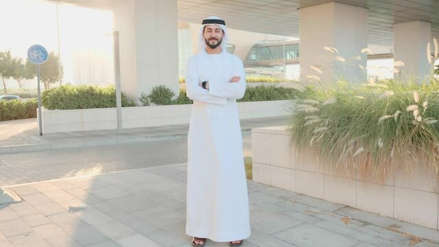Full body of Arab Emirates man. Standing UAE Middle Eastern local wearing Kandoora dish dash looking at a business location.
