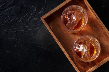 Whiskey in glasses with ice. Bourbon whisky on rocks on a black slate background, overhead flat lay...