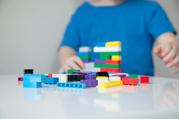 Naklejka premium Boy plays colorful multi-colored cubes and cars on the table. Early development and learning. 