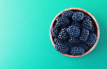 Blackberries in a wooden bowl. Ripe and tasty black berry isolated on green baclground.
