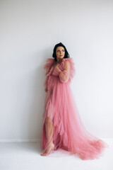 Beautiful pregnant woman in elegant dress posing to photographer in studio