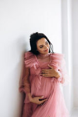 Beautiful pregnant woman in elegant dress posing to photographer in studio