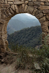 Fototapeta na wymiar Ruin of old stone arch in medieval town on peak of in Caucasian mountains in Dagestan as frame with view on landscape with green slopes mountains in canyon. Archeology adventure and tourist trip.
