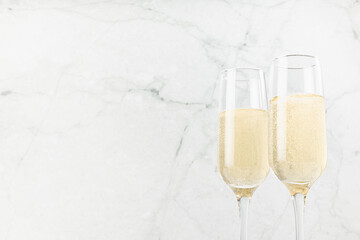 Fresh sparkling golden champagne in glasses on elegant soft light marble backdrop with refreshing beverage in summer sunlight, copy space, top part. Festive drink for celebration and cheers.