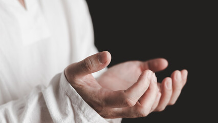 Naklejka premium An adult whose hand is prayed on the dark background.Respect for belief in religion and God. front view. peace concept.