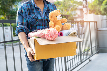 Holding clothing donation box with used clothes and doll at home to support help for poor people in...