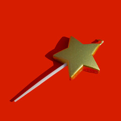 Cake candle in the form of a golden star with a shadow on a red background. New Year and Christmas concept