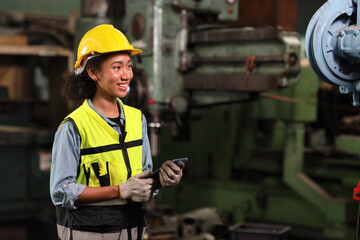 Technician engineer or worker in protective uniform standing and holding tablet while controlling operation or checking industry machine process with hardhat  at heavy industry manufacturing factory