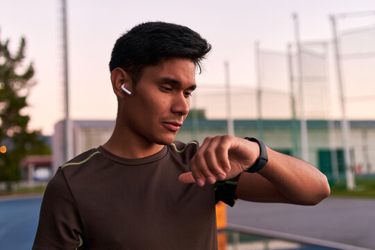 Young sportsman listening to music and checking his smartwatch