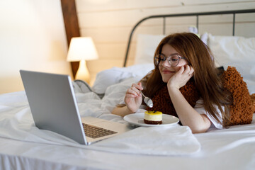 A girl in bed watches a series on a laptop with sweets. Leisure at home, watching movies.