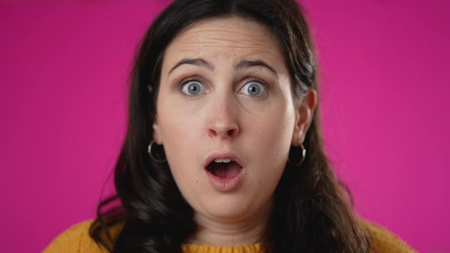 Closeup slow motion portrait of amazed young woman 20s shocked, saying WOW. Attractive lady surprised isolated on solid pink background.