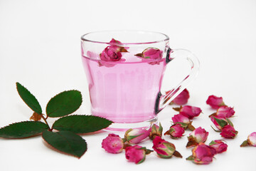 pink tea in a transparent glass mug and small buds of dry pink rose on a white background