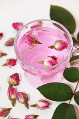 pink tea in a transparent glass mug and small buds of dry pink rose on a white background