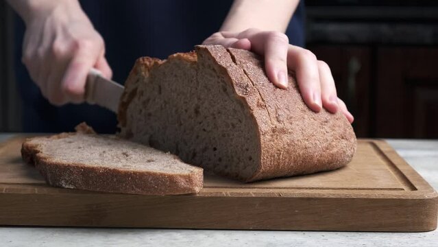 Woman's hands cutting whole grain wheat bread on wooden board with a white knife.