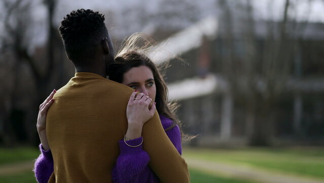 Interracial couple embrace outside. Young woman hugs partner