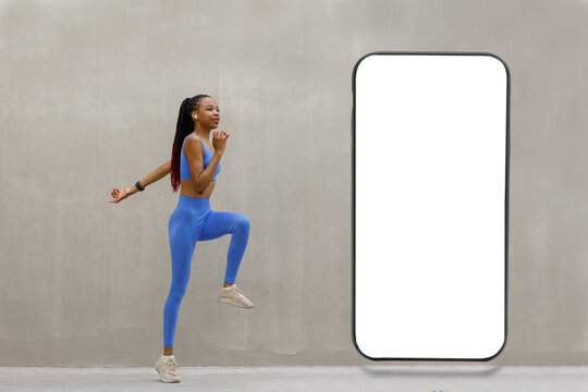 Sportswoman doing fitness in front of big giant smartphone with blank white screen on gray background presenting new cool app, free copy space mockup, website design banner
