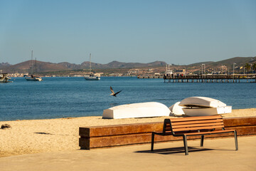 Sail boats (dinghies) parked on the beach by the Malecon in La Paz, Baja de California Sur, Mexico.  The historic Queen Elizabeth Dock is in the background, benches in foreground.