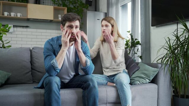 Irritated young woman screams in frustration offends abases her stressed disappointed husband in the living room at home Domestic psychological violence and emotional abuse against man