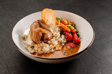 Dish of oatmeal with baked quail and vegetables on wooden background