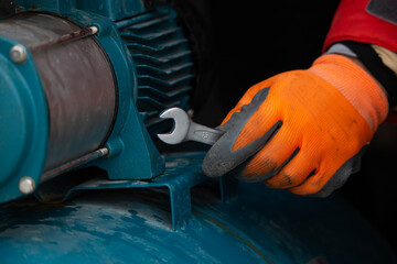 Man wearing orange work gloves repairing a water pump with metal wrench in his hand
