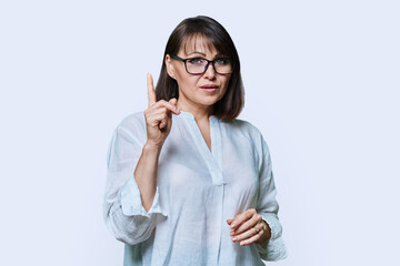 Middle aged serious woman showing index finger up, on white background