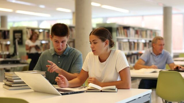 Female college student working on a project with a male student in the school library