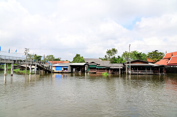 Fototapeta na wymiar BANGKOK, THAILAND - NOVEMBER 20, 2022 : Wooden houses, Thai houses and buildings along the Chao Phraya River with white clouds and blue sky background, Town Ayutthaya Waterfront, Thailand.