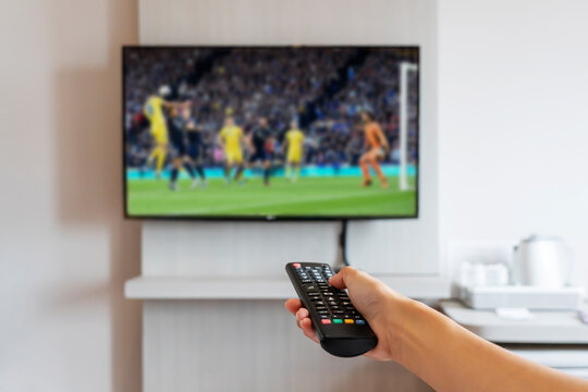 woman holding television remote control watching football program. Hands pointing to tv screen set and turning it on or off select channel watching tv in the home relax.