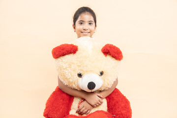 Happy indian girl kid hugging her big teddy bear isolated over beige studio background.