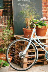 Fototapeta na wymiar Bicycle, cafe and small business outdoor restaurant or coffee shop for background in Paris with decoration, plants and menu board. Bike, carbon footprint and street, terrace or patio with wheel