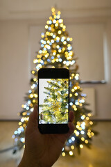 Man taking picture of Christmas tree decorated with a mobile phone