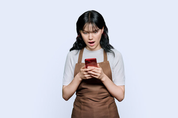 Surprised young woman in apron looking at smartphone screen