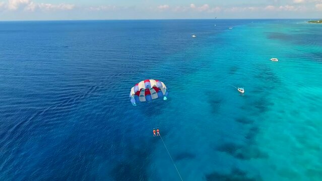 Parasailing aerial view. A couple paraskiing at tropical beach in bright day. 